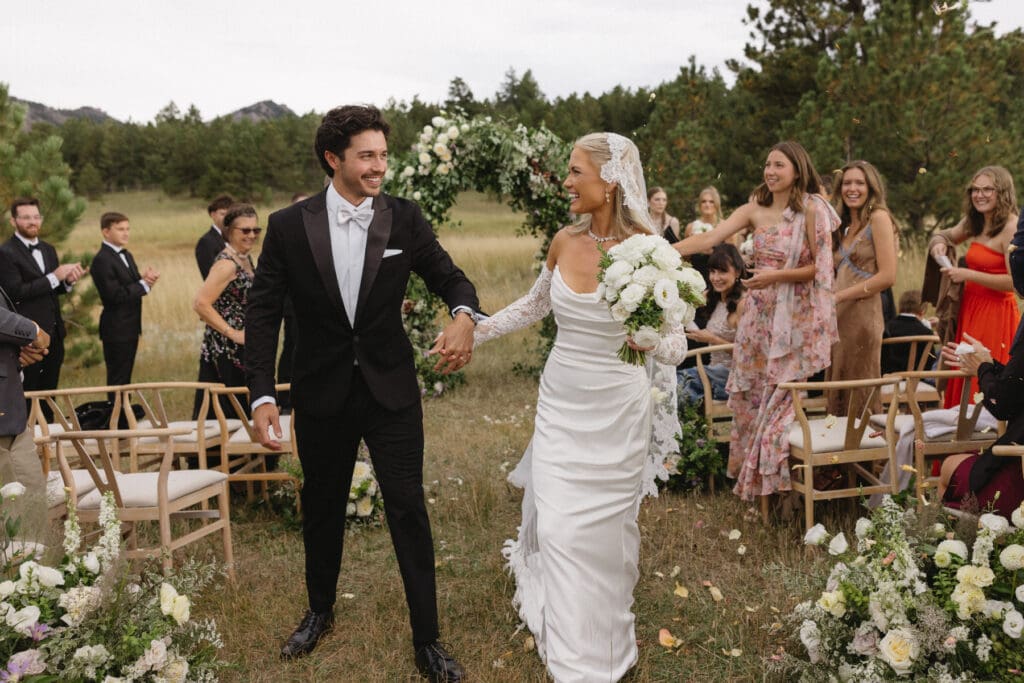 Newlyweds walking down the aisle after their outdoor wedding ceremony at Greystone Castle in Boulder, Colorado